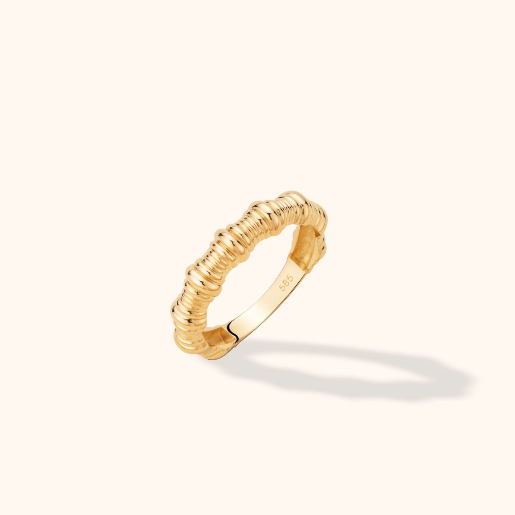 Gold-toned ring with repeating rounded ribs and a visible 585 stamp inside, tilted on a cream background with a soft shadow.