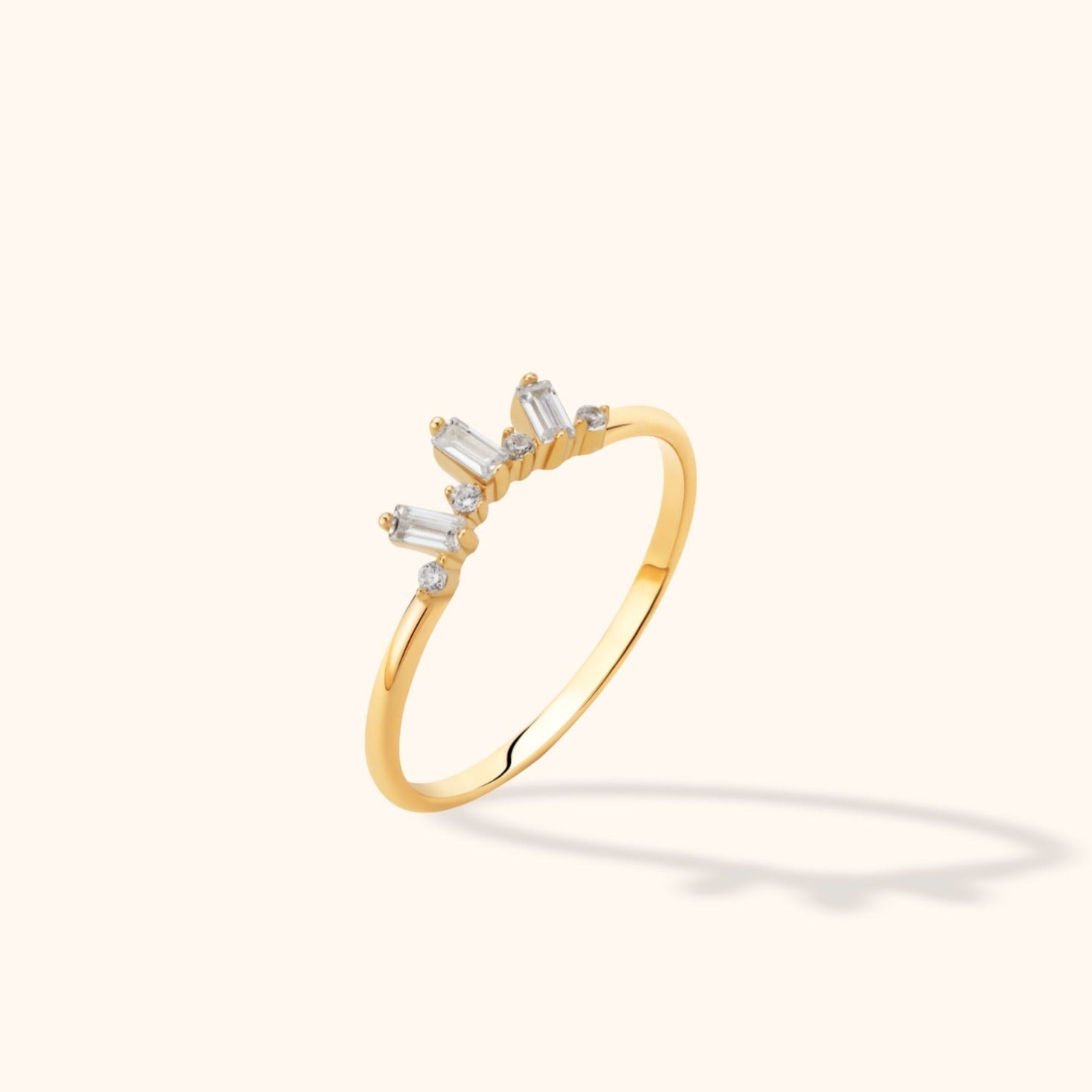 Gold-toned ring with a slim band and a crown-like row of three rectangular clear stones alternating with small round stones.