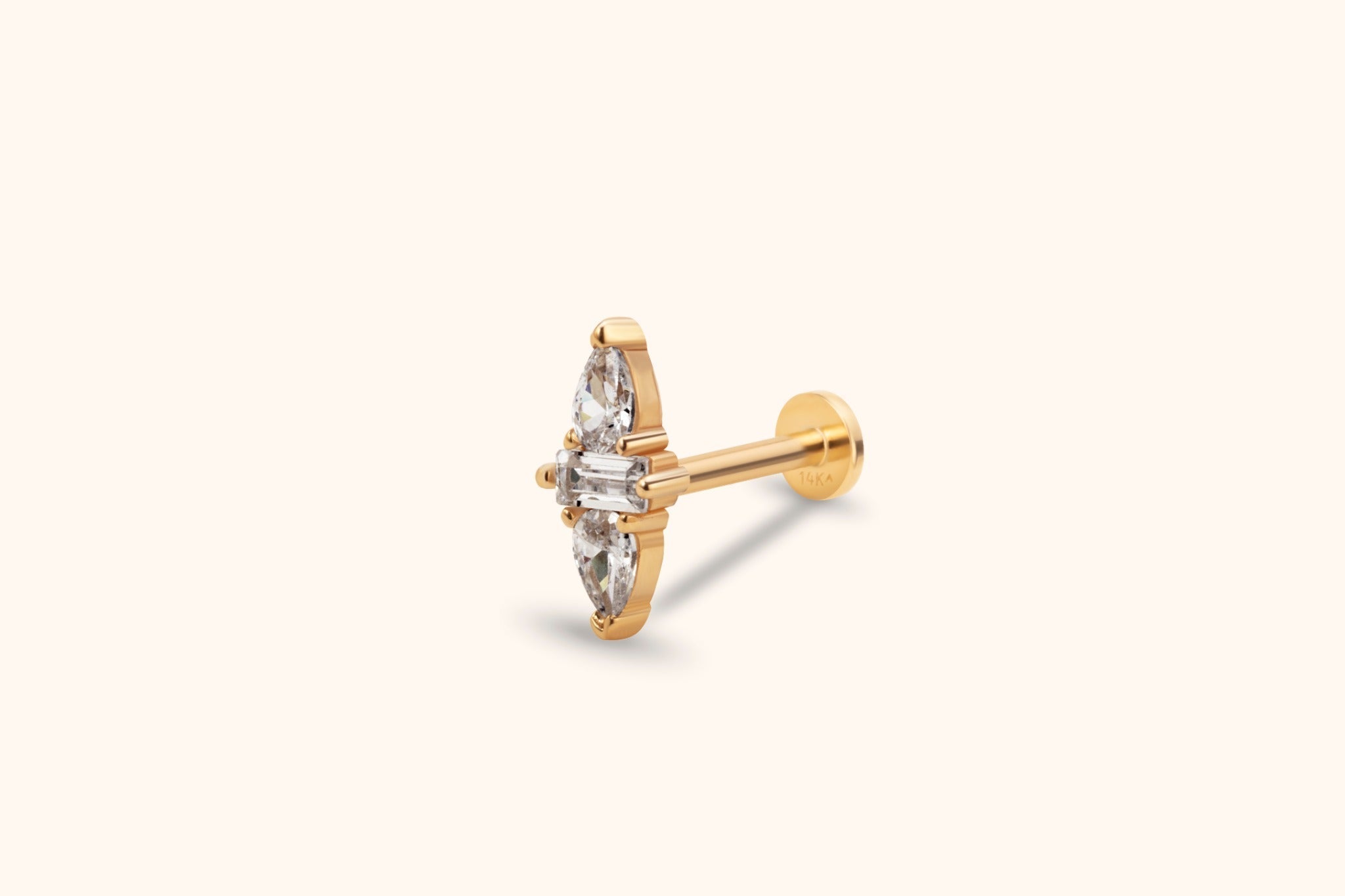 Gold-tone flat-back stud with a clear rectangular stone between two teardrop-shaped stones, shown at an angle on a cream background.