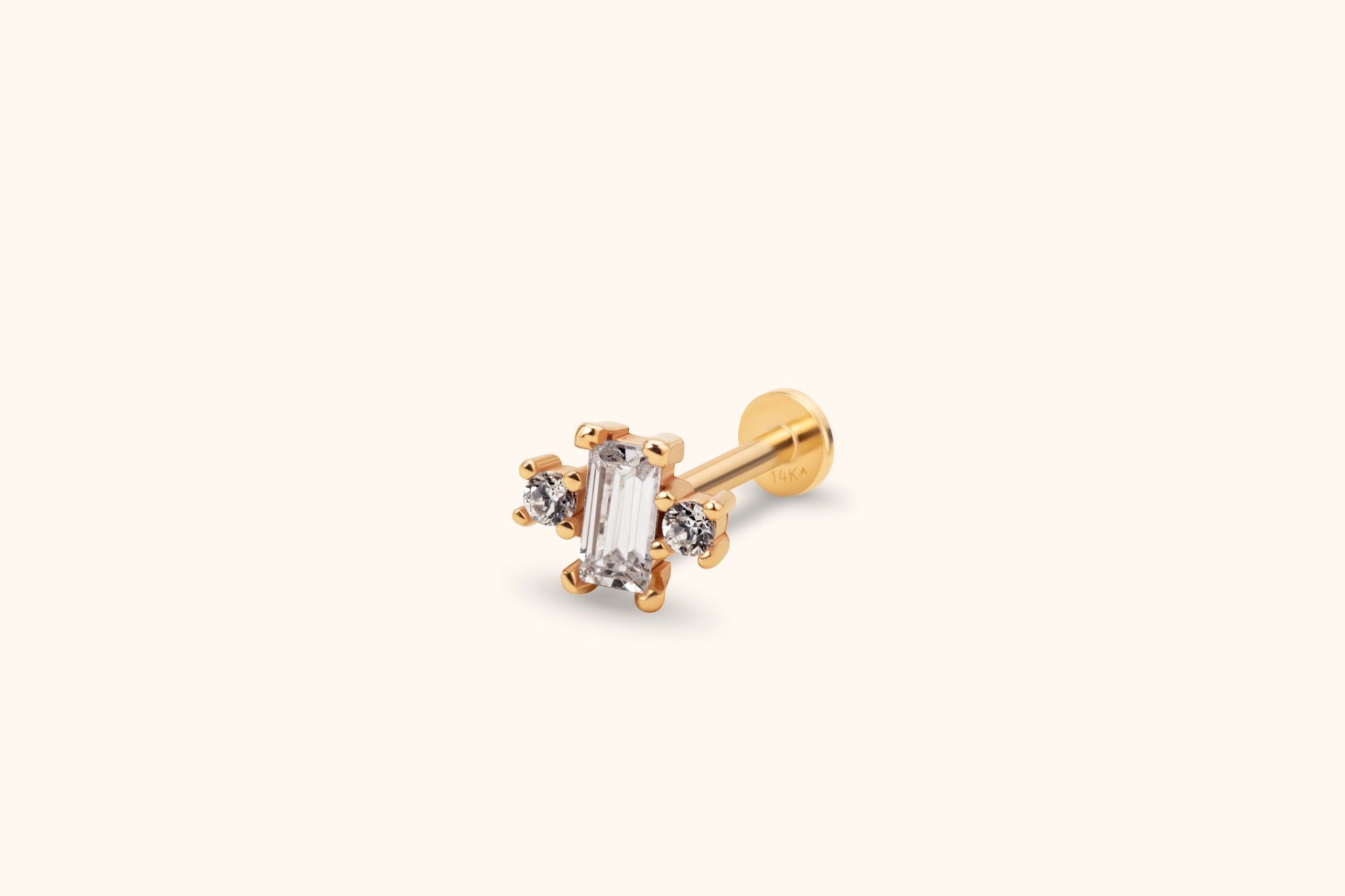 Gold-toned stud earring with a clear rectangular center stone flanked by two round stones, a straight post and flat disc back.