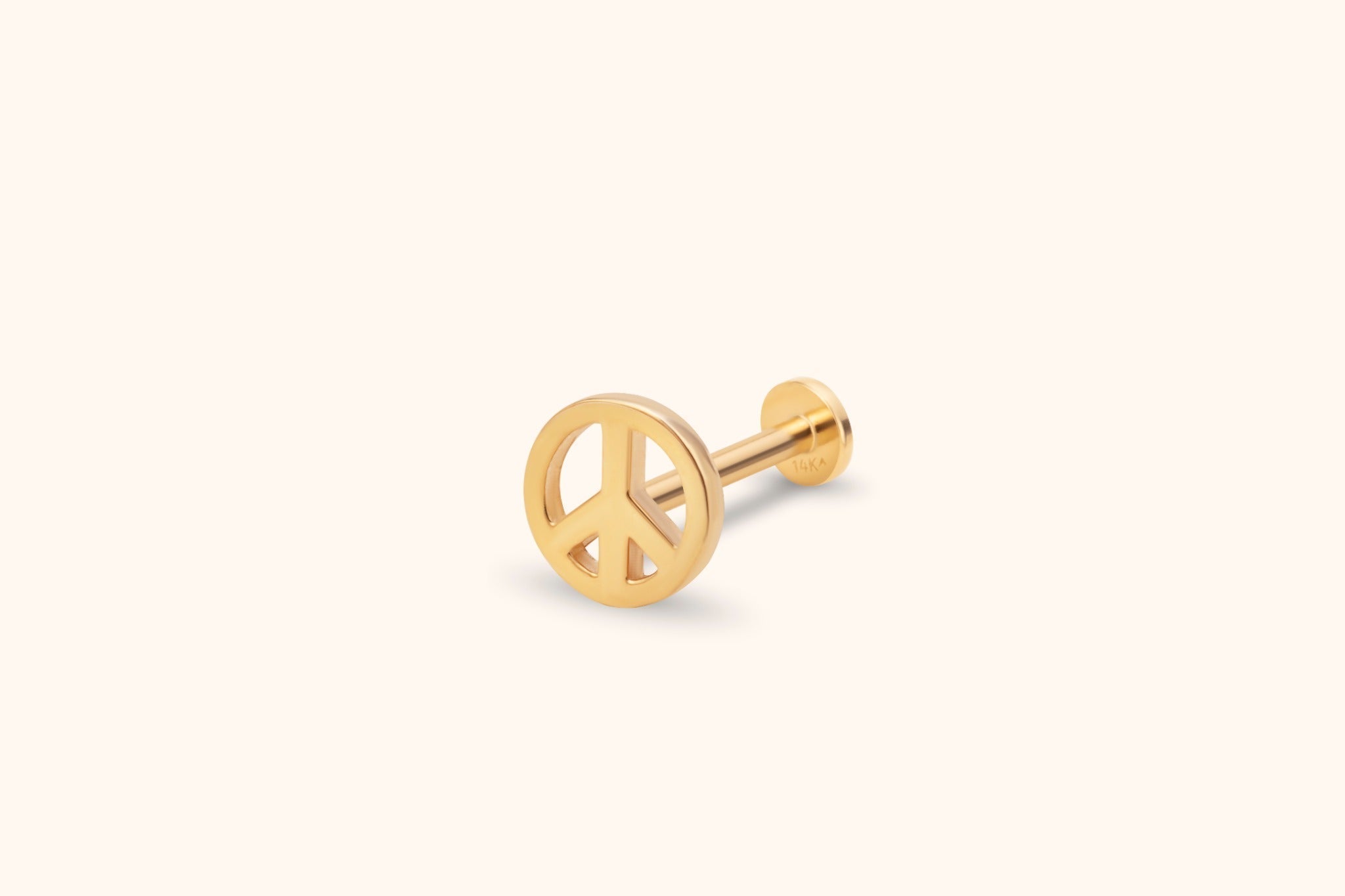 Gold-tone peace sign stud earring with a straight post and flat round back, shown at an angle on a pale cream background.