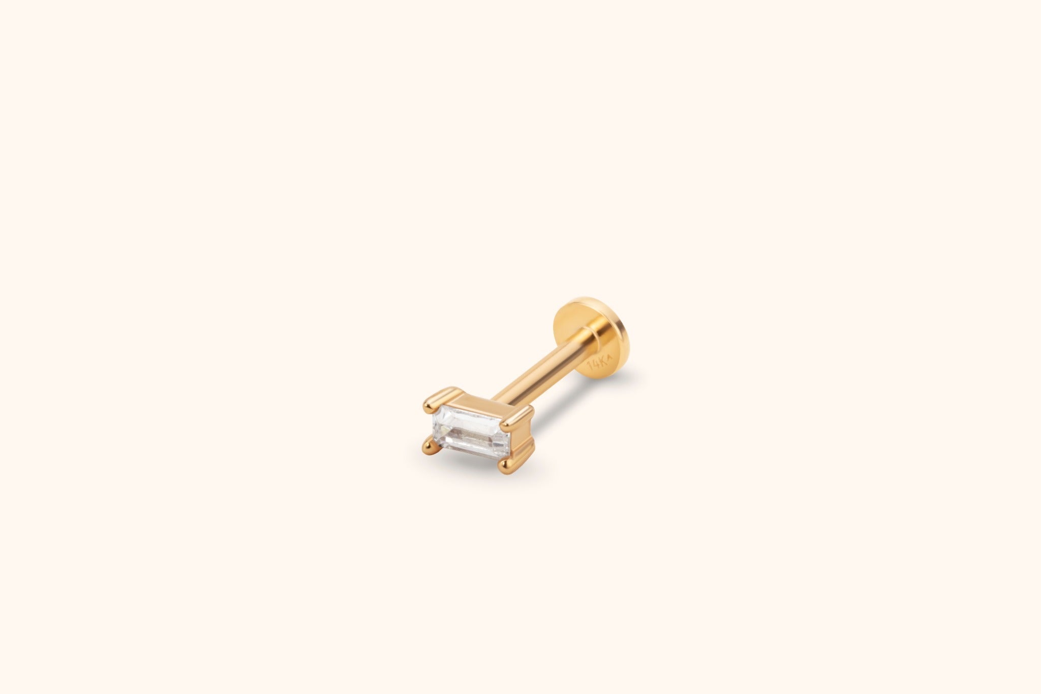 Gold-toned stud with a clear rectangular stone in a prong setting, a straight post and a flat round back on a cream background.