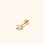 Gold-toned stud with a clear rectangular stone in a prong setting, a straight post and a flat round back on a cream background.