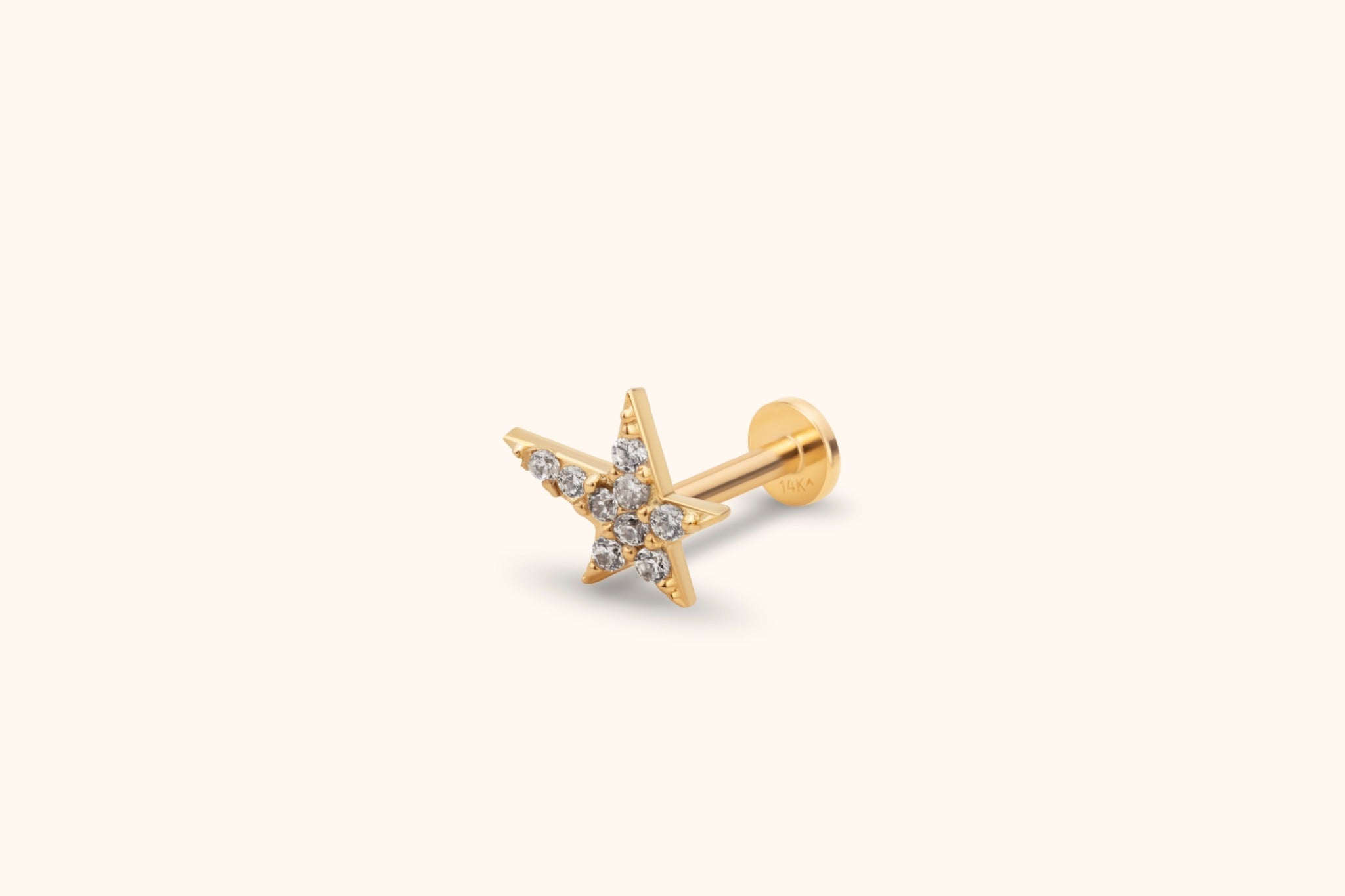 Gold-tone star stud earring with clustered clear round stones, a straight post and flat circular back on a cream background.