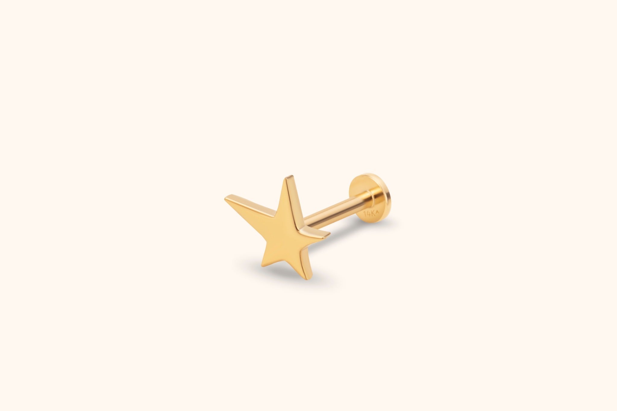 Gold-toned stud earring with a polished five-point star, straight post and round flat back on a pale cream background.