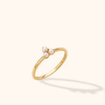 Slim gold-tone ring with three white pearl-like beads in a triangular cluster, shown at an angle on a cream background.