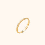 Slim gold-toned ring with a shiny twisted rope pattern, shown at an angle against a pale cream background.