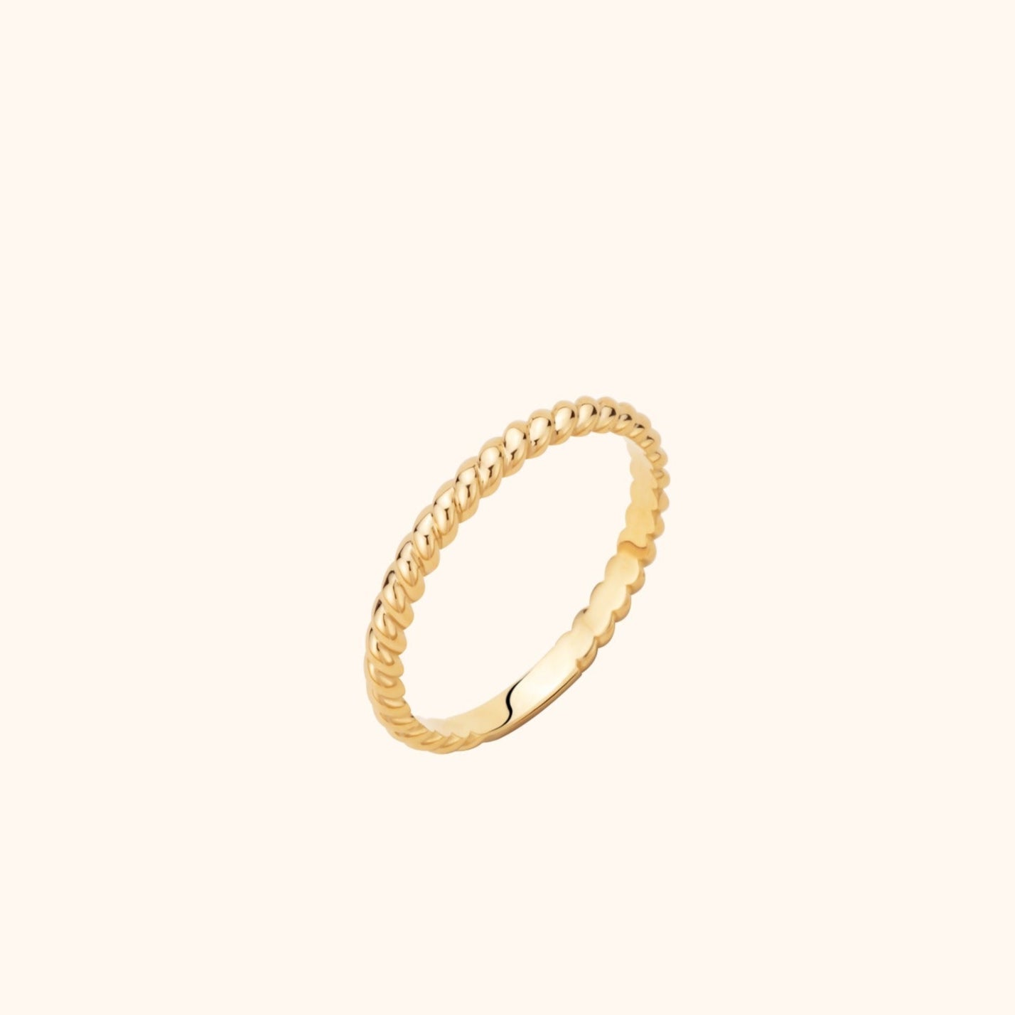 Slim gold-toned ring with a shiny twisted rope pattern, shown at an angle against a pale cream background.