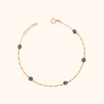 Gold-tone chain bracelet with five round blue faceted accents, a spring-ring clasp and extension links on a cream background.