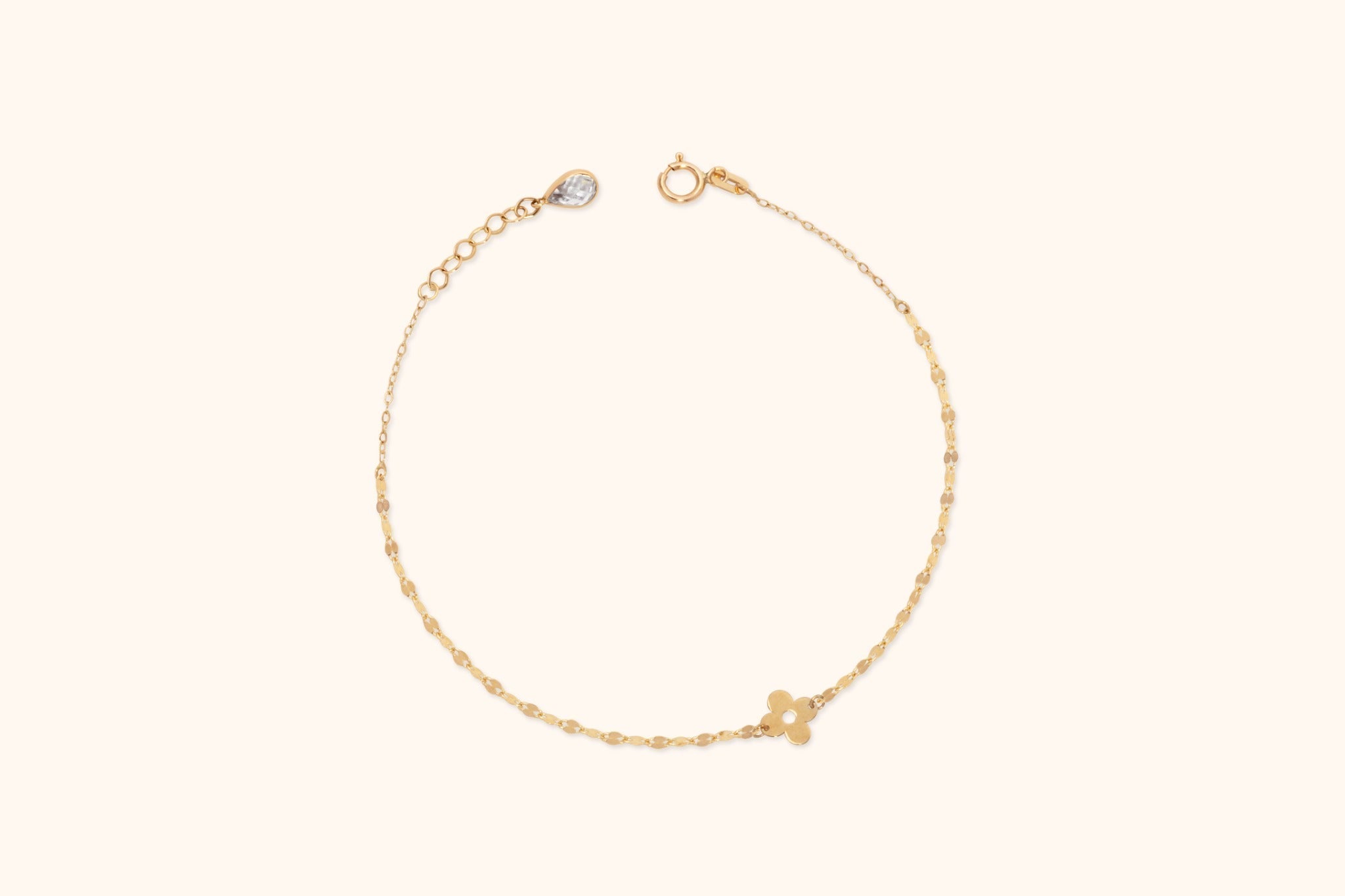 Gold-colored chain bracelet with a four-petal flower charm, round clasp, and extension chain ending in a clear teardrop-shaped detail.