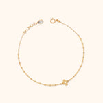 Gold-colored chain bracelet with a four-petal flower charm, round clasp, and extension chain ending in a clear teardrop-shaped detail.