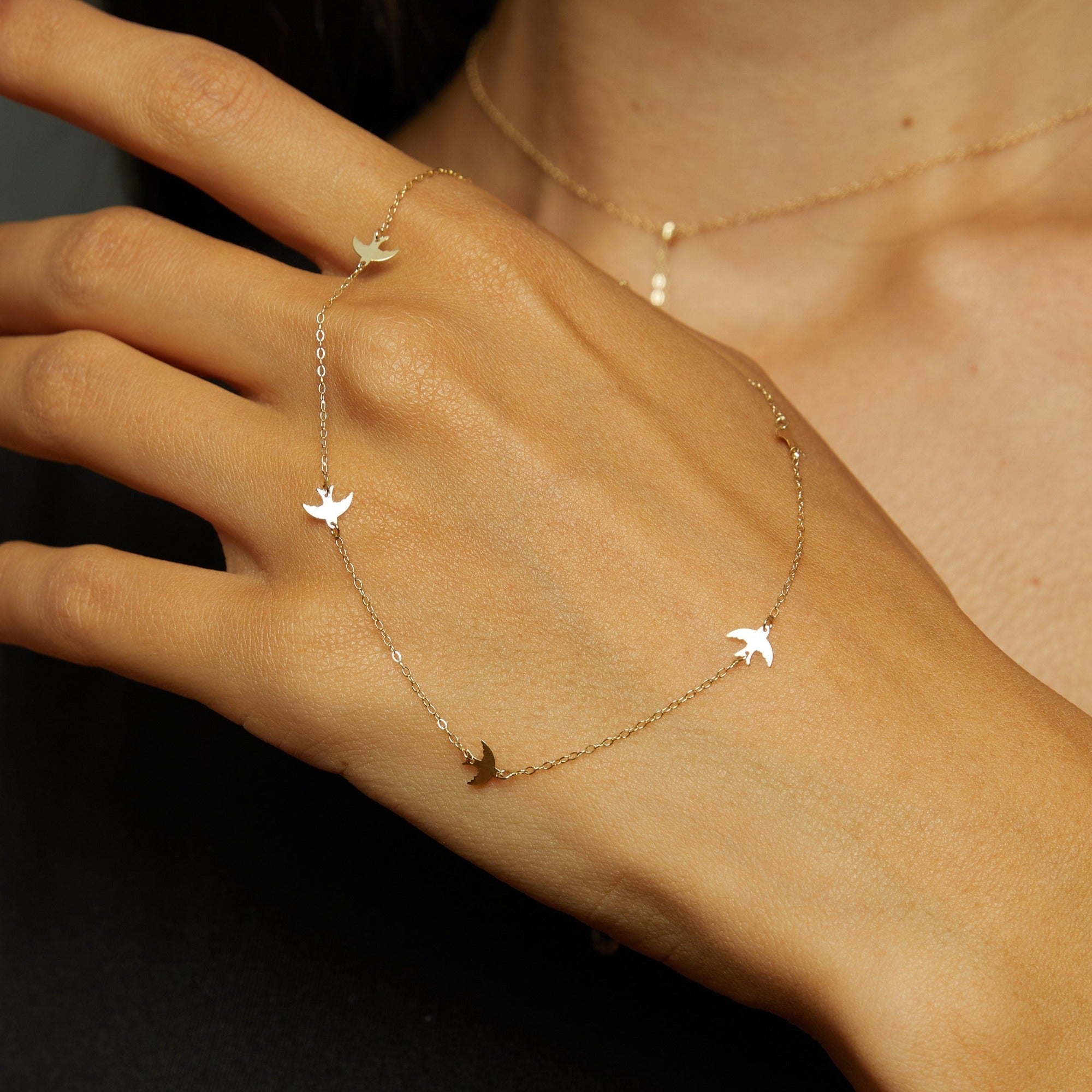 Fine gold-tone chain bracelet with four flat bird-shaped charms draped across the back of a hand.