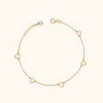 Gold-colored fine chain bracelet with five open heart links, a round clasp and an extension chain on a cream background.