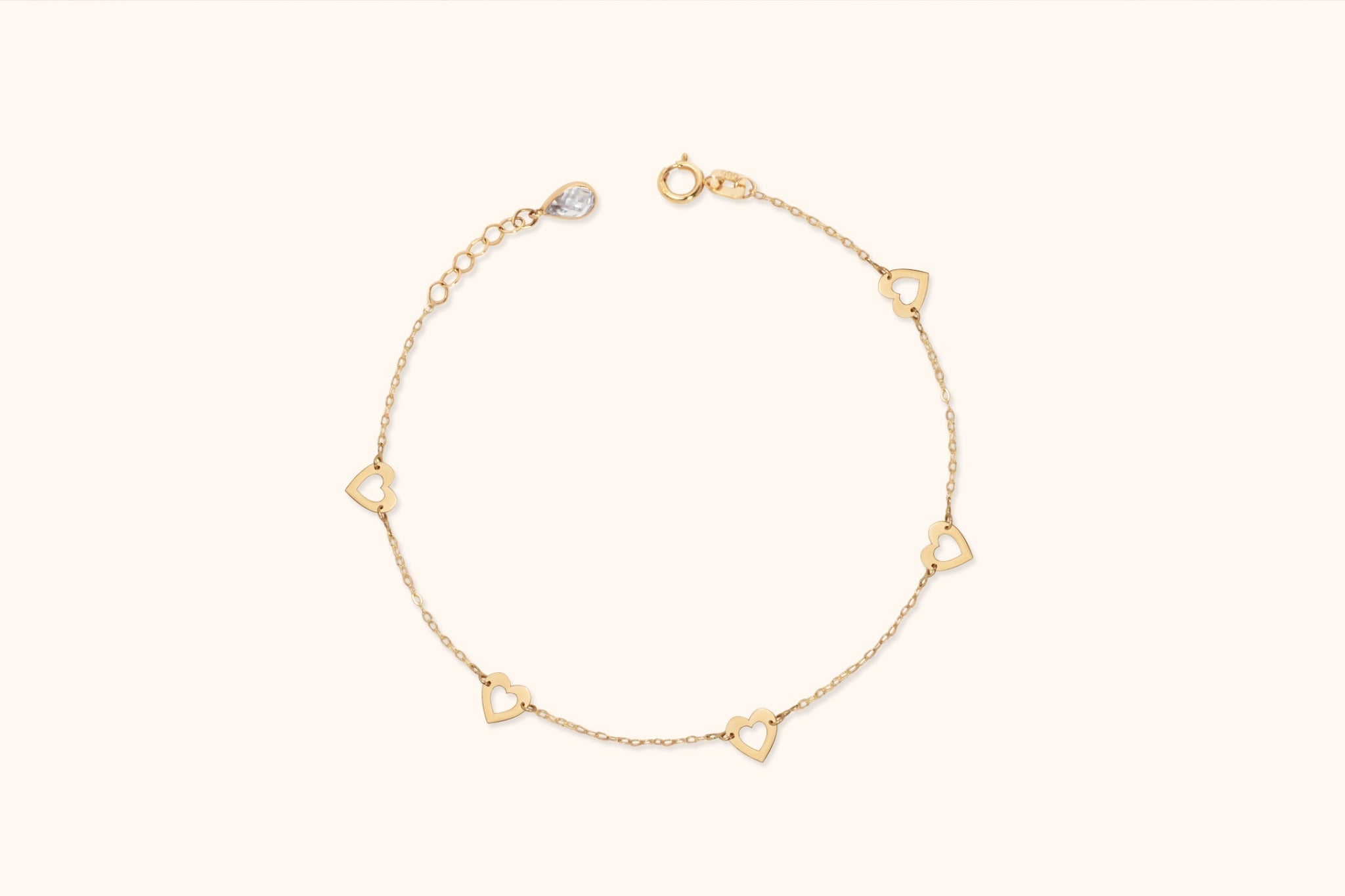 Gold-colored fine chain bracelet with five open heart links, a round clasp and an extension chain on a cream background.