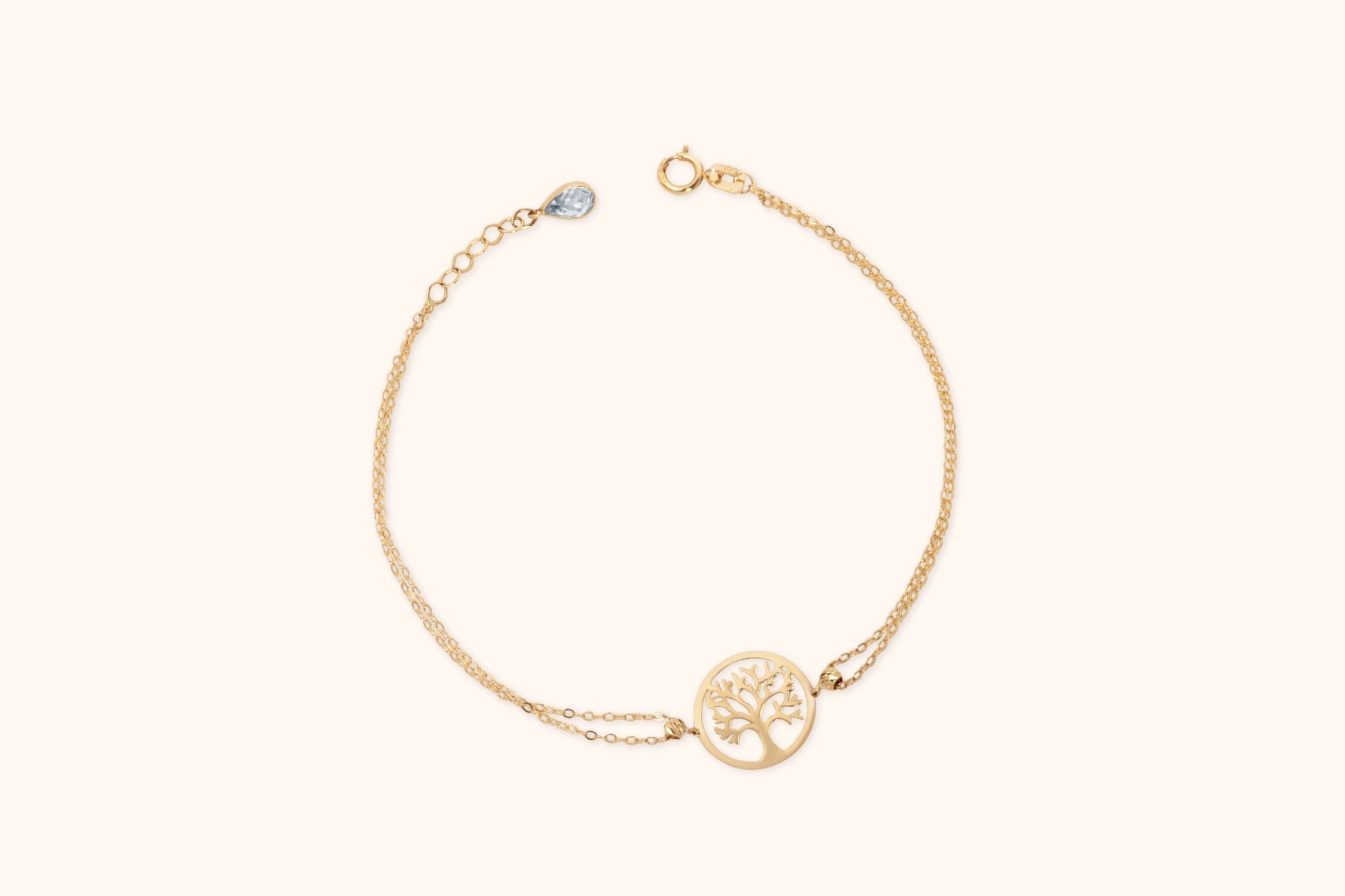 Gold-colored double-chain bracelet with a round tree cutout centerpiece, ring clasp and extension chain with a teardrop-shaped charm.