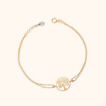 Gold-colored double-chain bracelet with a round tree cutout centerpiece, ring clasp and extension chain with a teardrop-shaped charm.