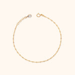 Fine gold-tone chain bracelet with flat oval links, a round clasp, extension chain and clear teardrop-shaped charm on a cream background.