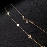 Gold-colored chain necklace with open and solid clover motifs, small textured beads and a round clasp on a black textured surface.
