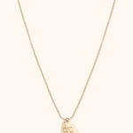 Gold-colored fine chain necklace with two overlapping elongated oval tags bearing the names Lucas and Olivia on a cream background.