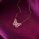 Gold-colored necklace with an openwork butterfly pendant and fine oval-link chain resting on deep magenta fabric.