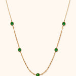 Gold-toned chain necklace with five faceted green accents in rounded settings and flat oval links along the lower section.