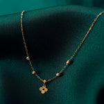 Gold-colored oval-link necklace with five textured beads and a four-lobed charm with a central hole, resting on dark teal fabric.