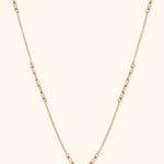 Gold-toned necklace with alternating sections of elongated paperclip links and fine oval links on a cream background.