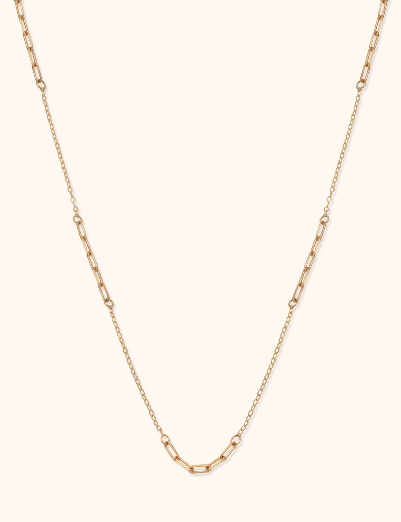 Gold-toned necklace with alternating sections of elongated paperclip links and fine oval links on a cream background.