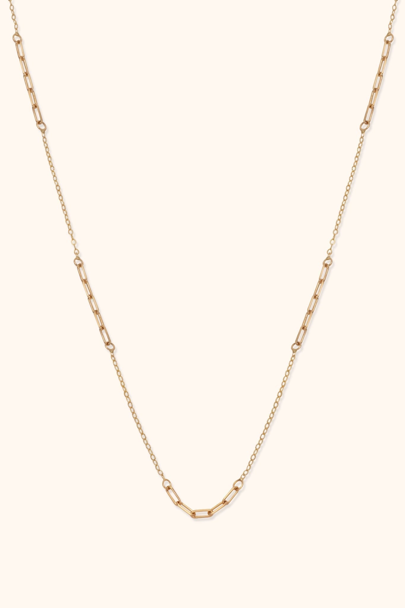 Gold-toned necklace with alternating sections of elongated paperclip links and fine oval links on a cream background.