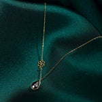 Gold-tone chain necklace with an open flower charm and faceted black teardrop pendant on dark green fabric.