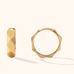 Two gold-colored hoop earrings with angular, faceted surfaces, shown from different angles against a cream background.