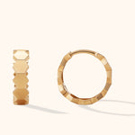 Two gold-toned hoop earrings with polished hexagonal facets, shown from different angles on a pale cream background.