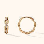 Two gold-toned chain-link hoop earrings with rows of clear round accents, shown from different angles on a cream background.