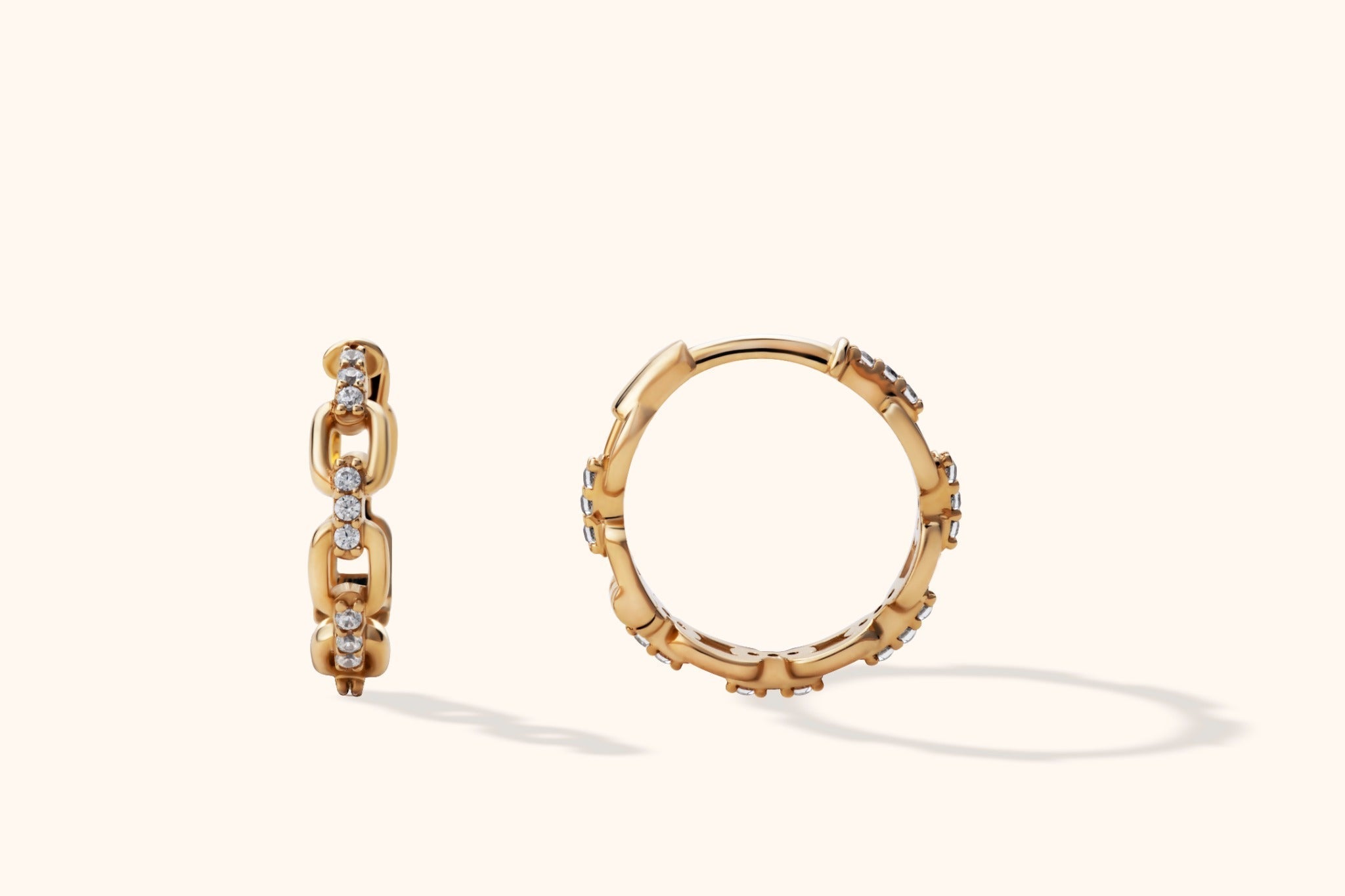 Two gold-toned chain-link hoop earrings with rows of clear round accents, shown from different angles on a cream background.
