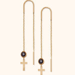 Pair of gold-tone threader earrings with long fine chains, round black faceted accents and flat cross pendants on a cream background.