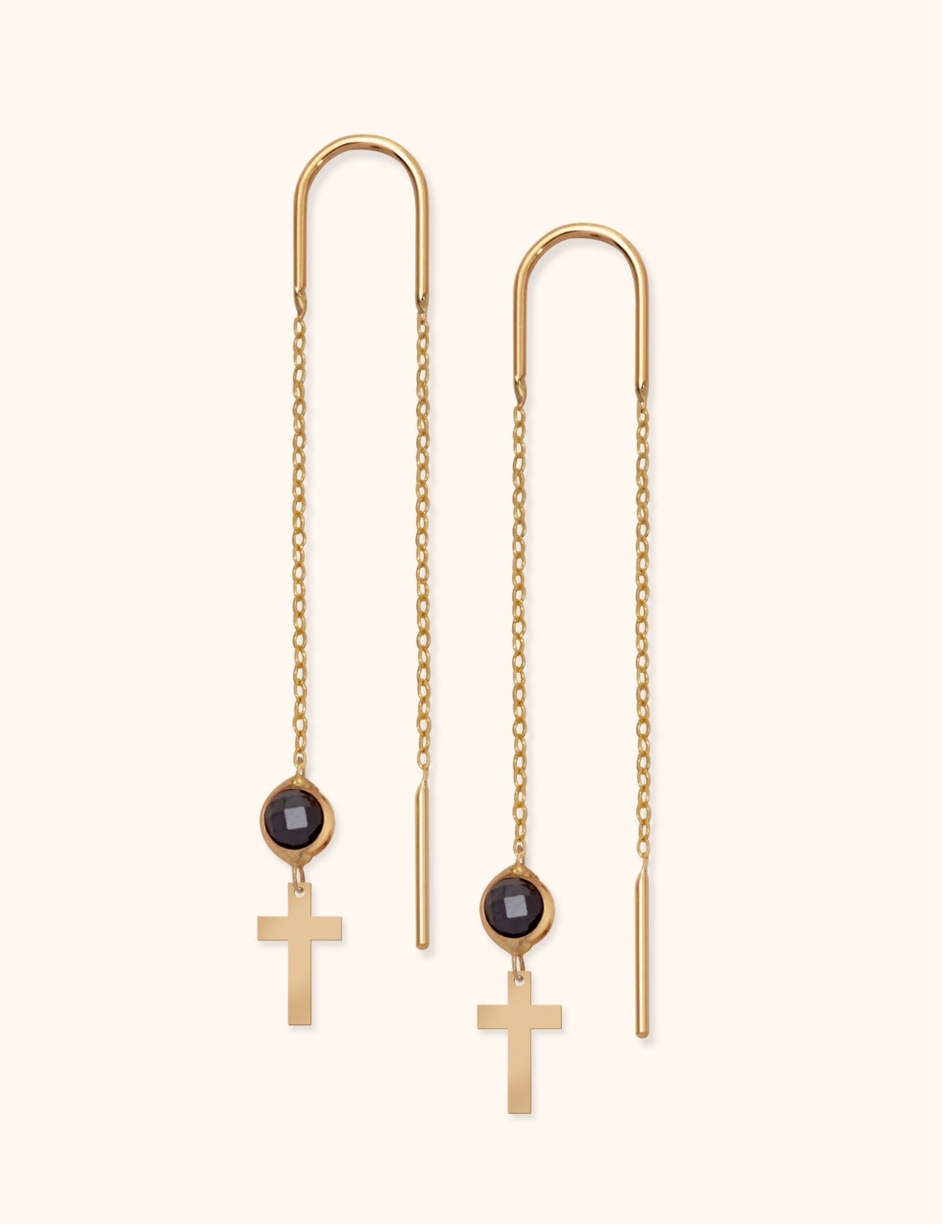 Pair of gold-tone threader earrings with long fine chains, round black faceted accents and flat cross pendants on a cream background.