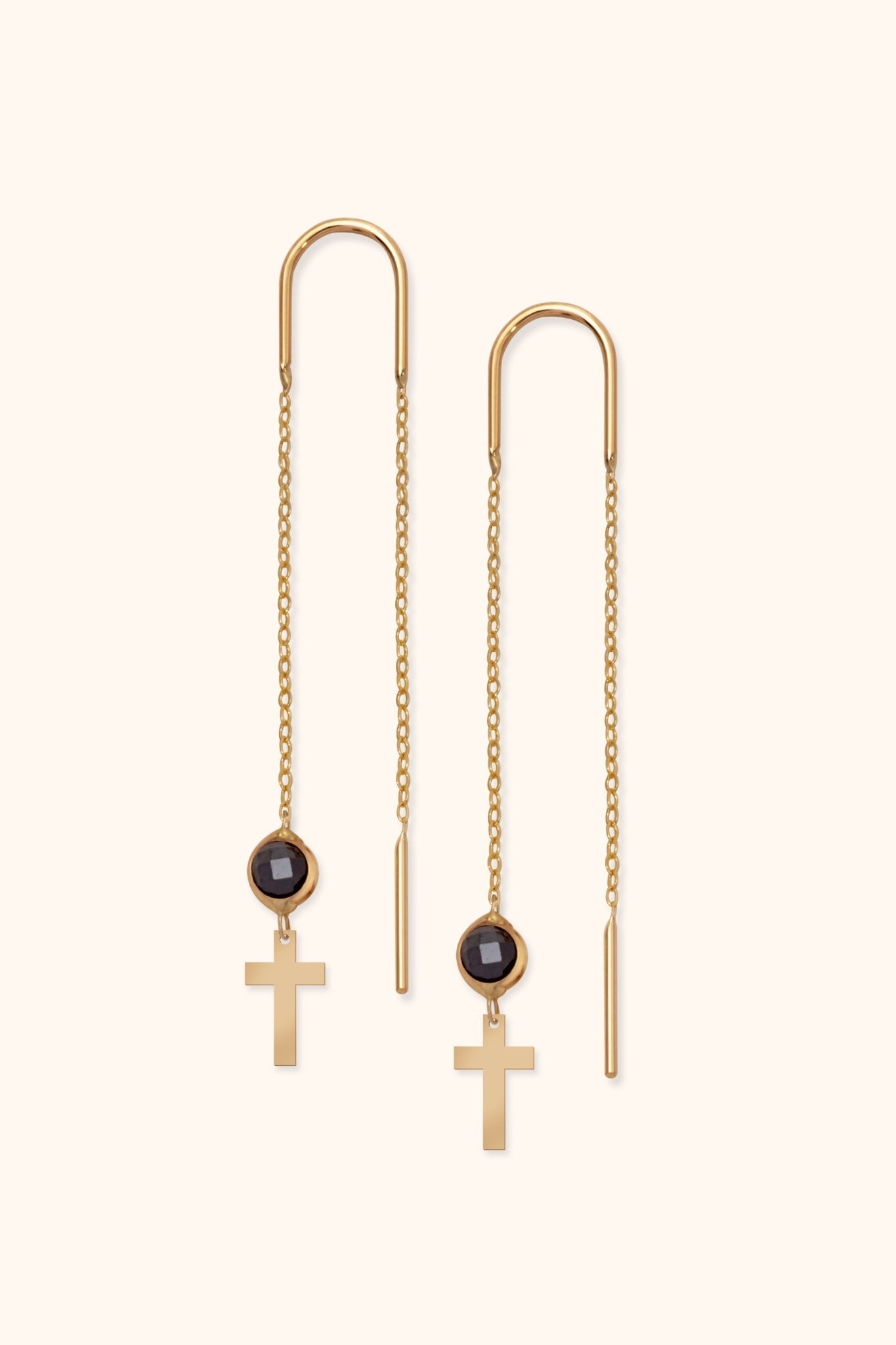 Pair of gold-tone threader earrings with long fine chains, round black faceted accents and flat cross pendants on a cream background.