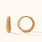 Two gold-colored hoop earrings with rounded ribs, shown from different angles on a pale cream background.