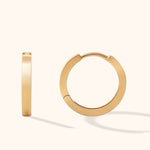 Two smooth gold-colored hoop earrings, one viewed edge-on and the other showing its circular shape, on a cream background.