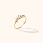 Gold-toned ring with a slim band and an asymmetric cluster of clear round stones, including a larger raised center stone.