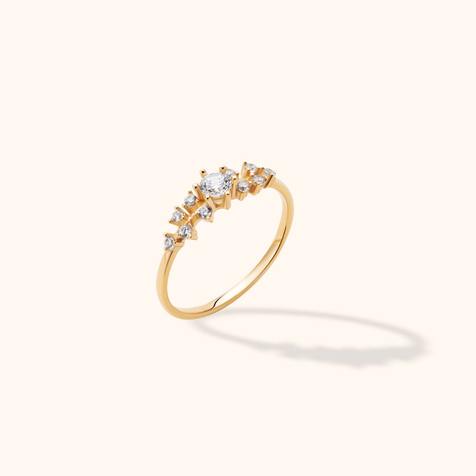 Gold-toned ring with a slim band and an asymmetric cluster of clear round stones, including a larger raised center stone.