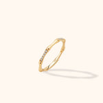Gold-toned ring with a slender bamboo-like band and rows of small clear stones, shown tilted on a cream background.