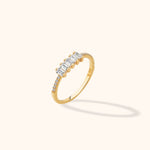 Gold-toned ring with five clear rectangular stones across the top and small round stones along both sides of a slim band.