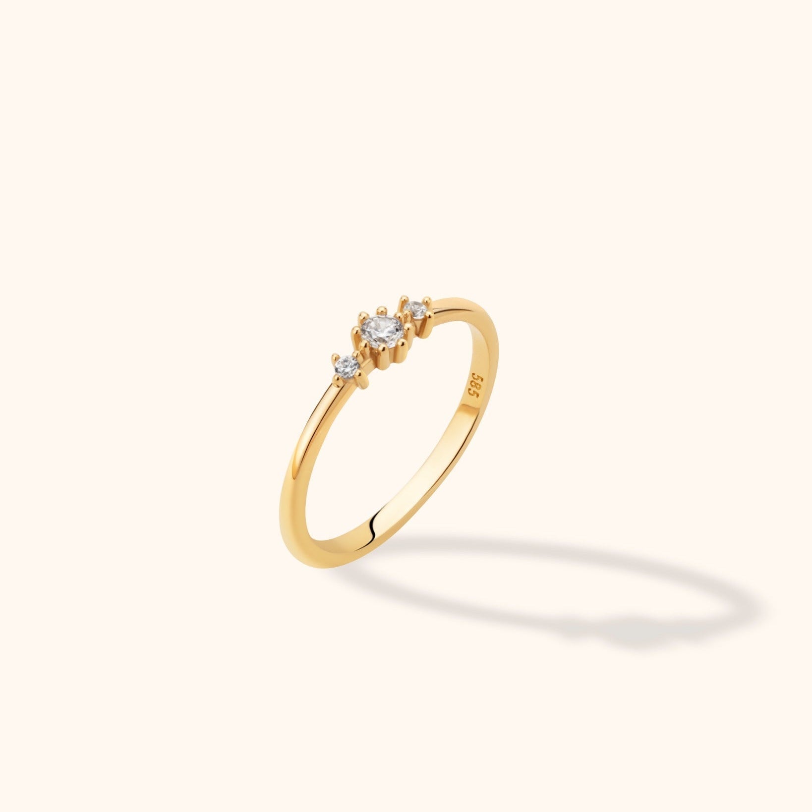 Slim gold-toned ring with three round clear stones in prong settings, a larger center stone, and a polished band shown at an angle.