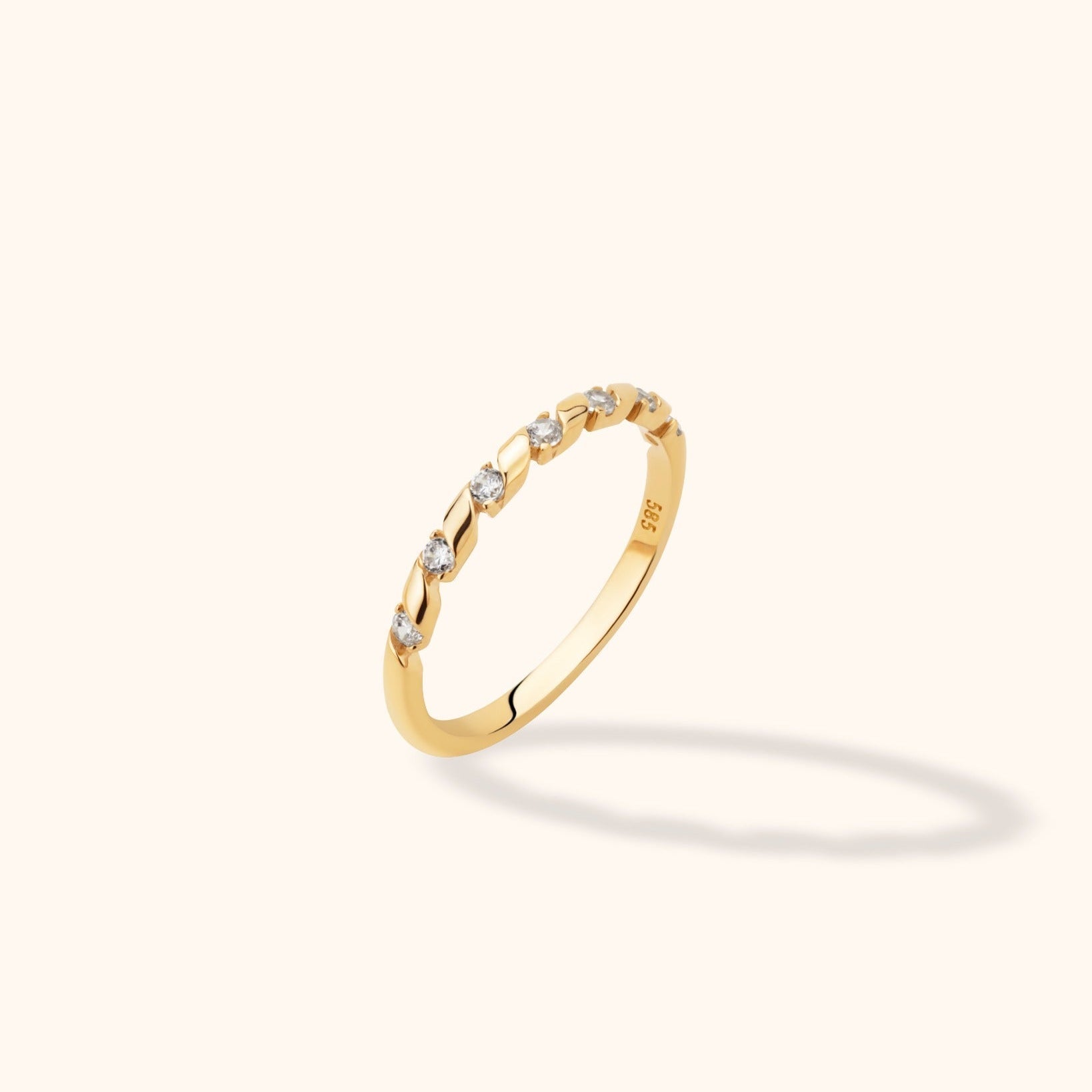 Slim gold-toned ring with alternating twisted sections and round clear stones along the upper band, shown at an angle.