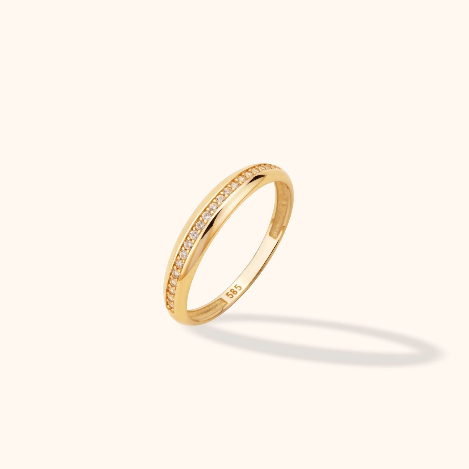 Slim gold-colored ring with a row of small clear stones between polished edges, shown at an angle with a visible 585 stamp inside.