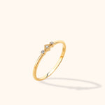 Slim gold-colored ring with three clear accents in a central diamond-shaped setting and two round settings, shown at an angle.