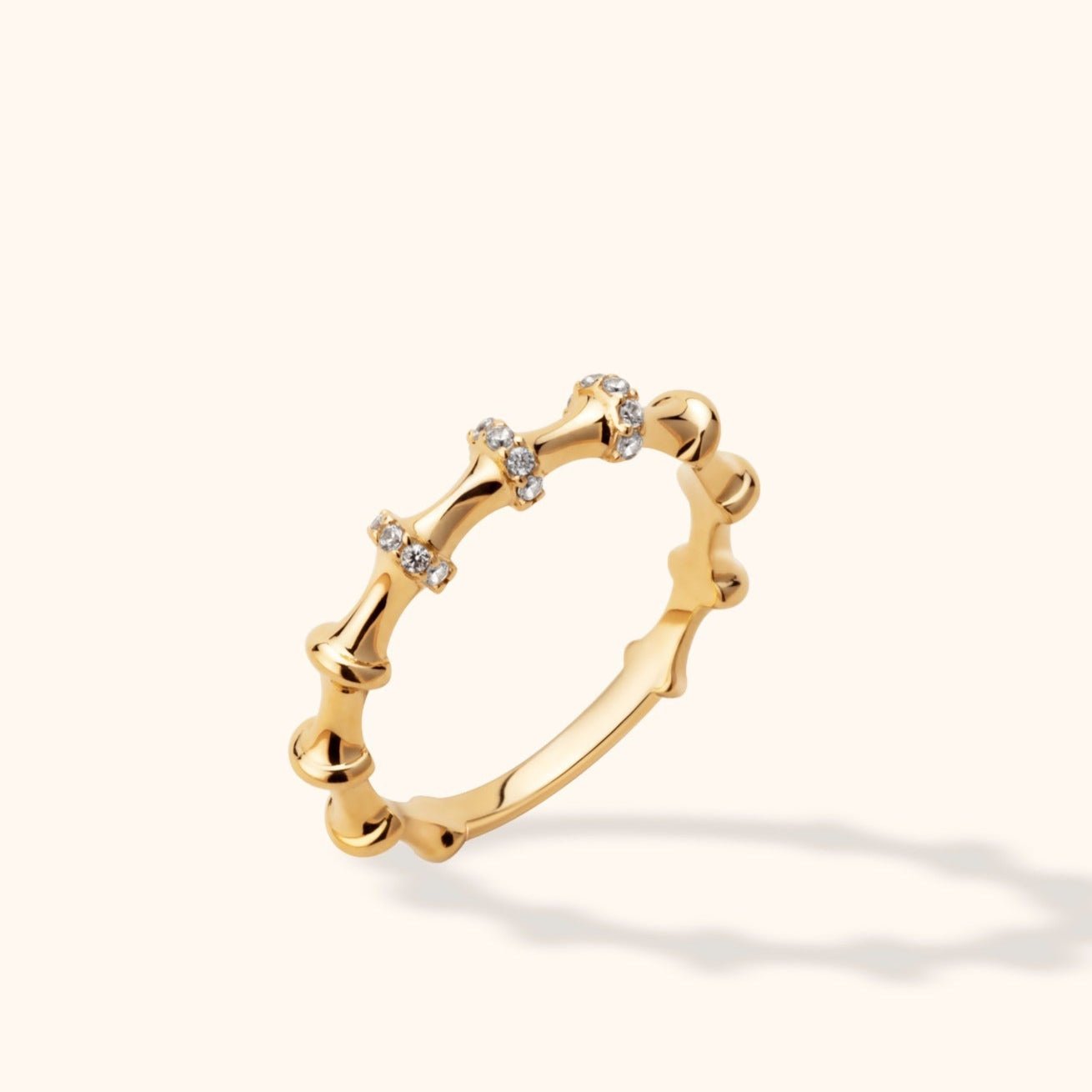 Gold-colored ring with bamboo-like segments and small clear accents, shown tilted against a pale cream background.