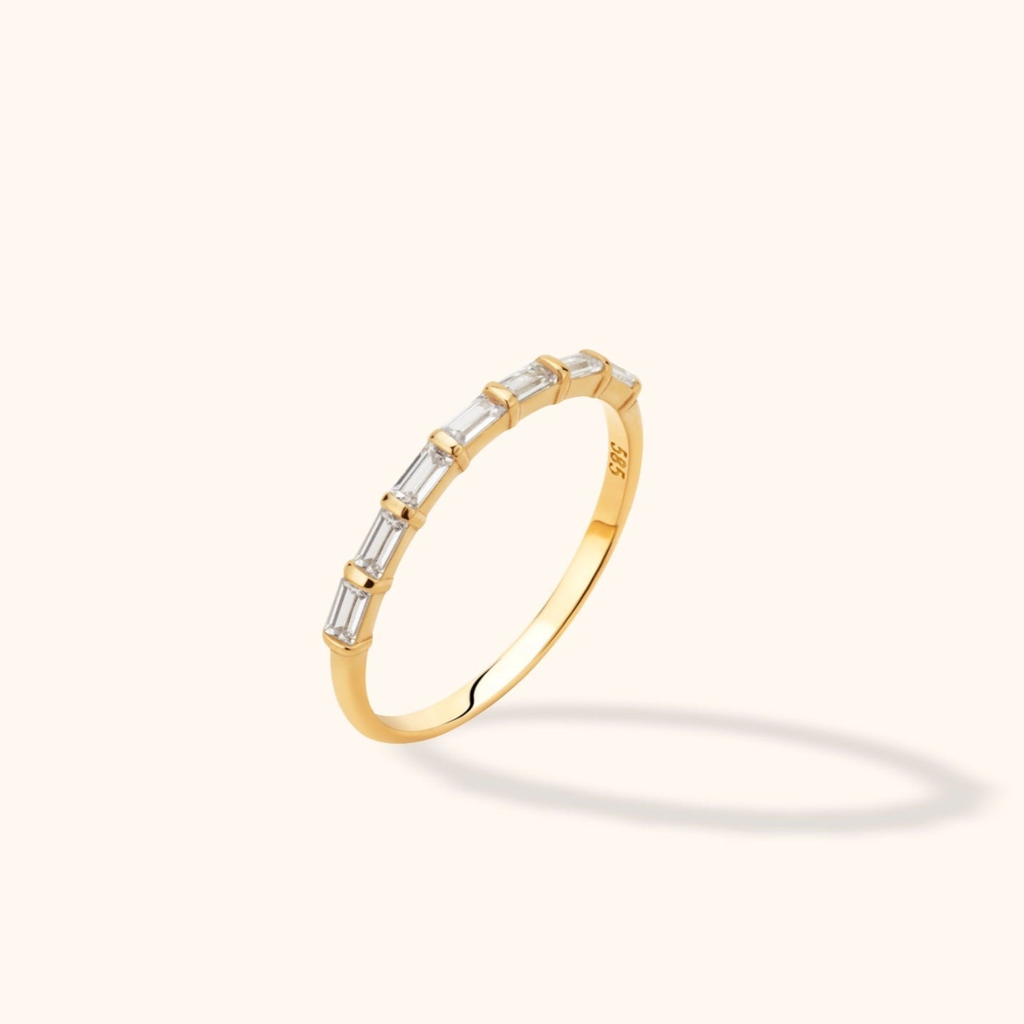 Slim gold-colored ring with a row of clear rectangular stones separated by narrow bars, shown at an angle on a cream background.