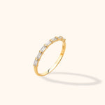 Slim gold-colored ring with a row of clear rectangular stones separated by narrow bars, shown at an angle on a cream background.